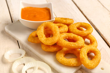 Board with fried breaded onion rings and sauce on white wooden background