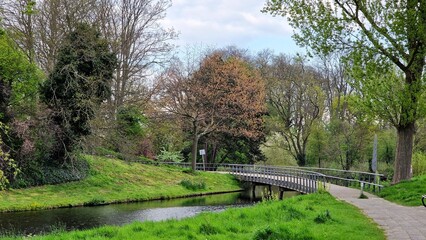 Fototapeta na wymiar Beautiful spring landscape in the city park, with a footbridge over a canal, trees and green grass.