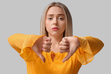 Young woman showing dislike on light background, closeup