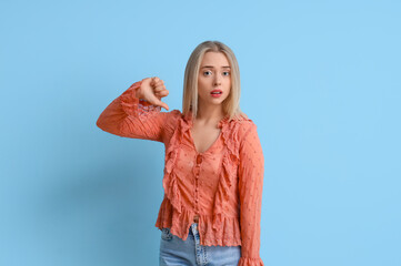 Upset young woman showing dislike on blue background