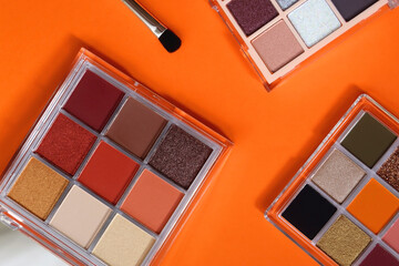 Colorful eyeshadow palettes and make up brush on orange background. Top view. 