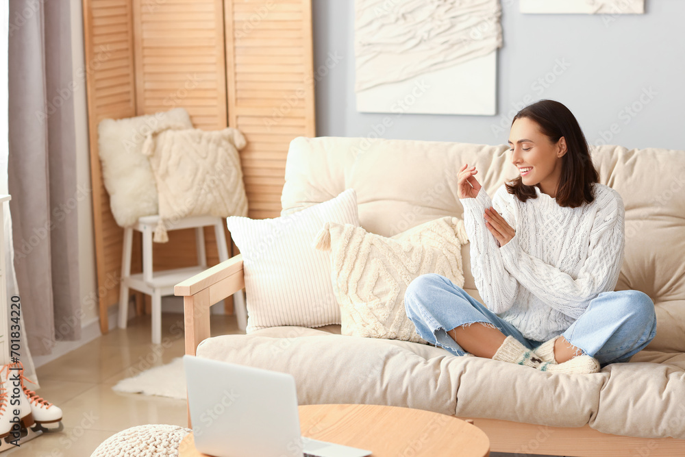 Wall mural young woman in warm sweater sitting on sofa at home