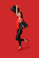 Beautiful young Asian woman with shopping bags on red background. Black Friday sale