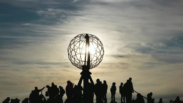 Nordkapp at Sunset with Colorful Clouds and Silhouette of Globe Monument and people. Globe monument at North Cape at midnight, island of Mageroya, Norway