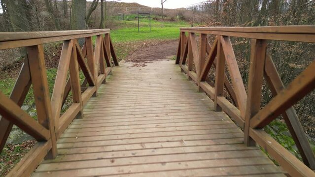 pedestrian bridge over a small gorge and a stream. it consists of two steel crossbeams. as the surface and railing of the bridge is made of brown painted planks. is long and narrow. in the wild