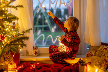 Cute child, sitting on a window, looking outdoors for Santa Claus.