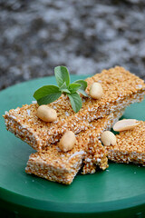 closeup the bunch sesame with dark sugar sweat and pea nut seeds ,green mint on the green plastic box soft focus natural grey brown background.