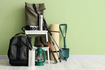 Fotobehang Set of camping equipment with backpack, oil lantern and outdoor gear near green wall © Pixel-Shot