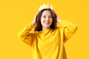 Young Asian woman in paper crown on yellow background