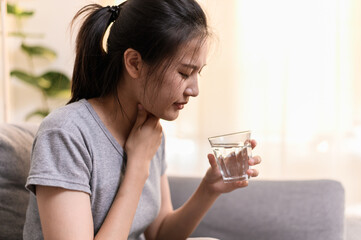 Young Asian woman have a sore throat or have a sick fever taking a medicine and drinking water...