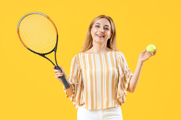 Mature woman with tennis racket and ball on yellow background