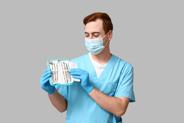 Male dentist in mask with set of dental tools on grey background. World Dentist Day