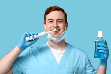Male dentist with electric toothbrush and bottle of mouth rinse on blue background. World Dentist...