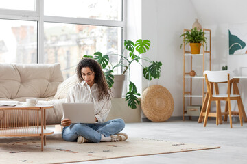 Young African-American woman using laptop on floor at home