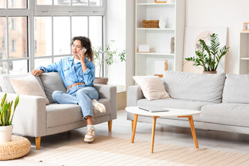 Young African-American woman talking by mobile phone on sofa at home
