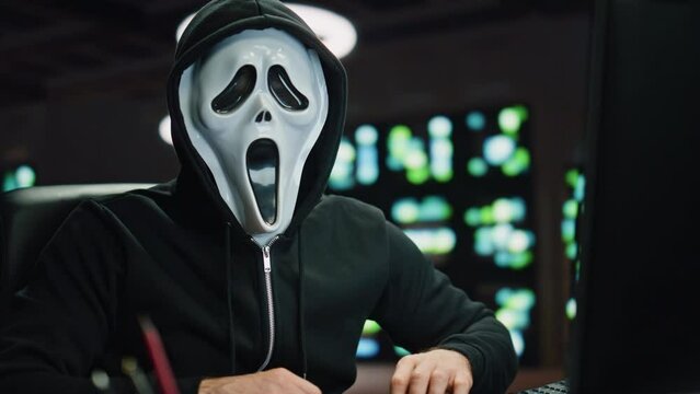 Anonymous hacker breaking data servers at night room closeup. Man looking camera