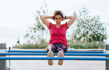 Determined woman doing sit-ups on outdoor fitness equipment with natural scenery in the background