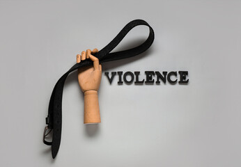Wooden hand with belt and word VIOLENCE on light background