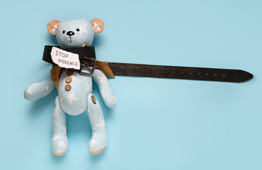 Paper with text STOP VIOLENCE, belt and toy bear on blue background