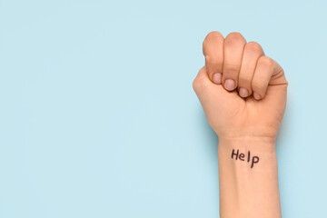 Woman with clenched fist and written word HELP on blue background. Domestic violence concept