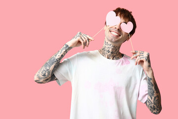 Funny young man with paper hearts on pink background