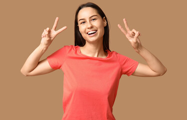 Beautiful young woman showing victory gesture on beige background