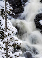 Small winter waterfall cascades over rocks past snow covered rocks in Yellowstone National Park