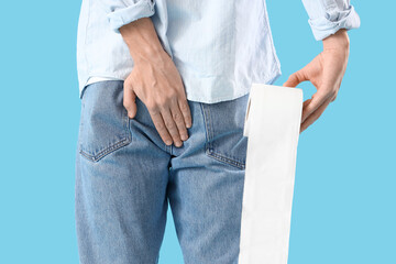 Young man with hemorrhoids and toilet paper on blue background, back view