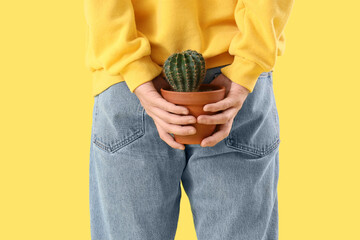 Young man with hemorrhoids and cactus on yellow background, back view