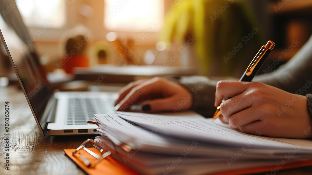 Poster hands of a person typing on a laptop keyboard with a blurred background of stacked files and documen