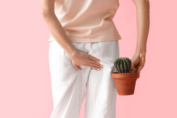Young woman with hemorrhoids and cactus on pink background, back view