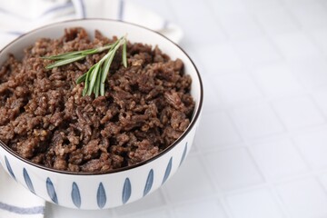 Fried ground meat in bowl and rosemary on white tiled table, closeup. Space for text
