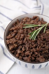Fried ground meat in bowl and rosemary on white tiled table, closeup
