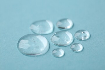 Drops of cosmetic serum on light blue background, closeup