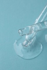 Dripping cosmetic serum from pipettes onto light blue background, macro view