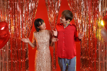 Young couple with tinsel on red background. Valentine's Day celebration