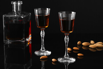 Liqueur glasses with tasty amaretto, bottle and almonds on black table, closeup