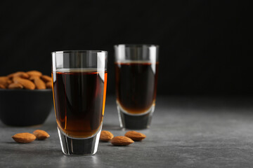 Glasses with tasty amaretto liqueur and almonds on gray table, closeup. Space for text