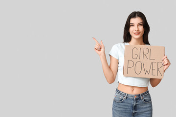 Young woman holding cardboard with text GIRL POWER and pointing at something on grey background....