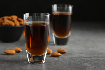 Glasses with tasty amaretto liqueur and almonds on gray table, closeup. Space for text