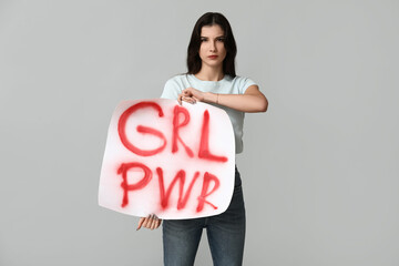 Young woman holding sign with text GRL PWR on grey background. Feminism concept