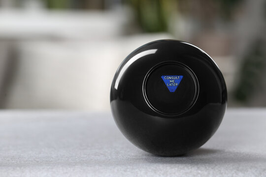 Magic eight ball with prediction Consult Me Later on light gray table, closeup. Space for text
