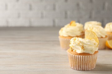 Tasty cupcake with cream, zest and lemon slice on light wooden table. Space for text