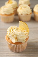 Tasty cupcake with cream, zest and lemon slice on light wooden table, closeup