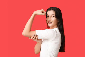 Young woman flexing muscles on red background. Feminism concept
