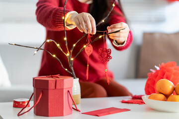 Asian Woman decorated house for Chinese New Year Celebrations. putting traditional pendant to the...