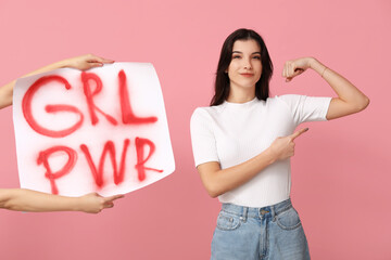 Young woman with sign GRL PWR pointing at her muscles on pink background. Feminism concept