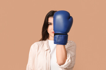 Young woman in boxing gloves on beige background. Feminism concept
