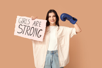 Young woman with sign GIRLS ARE STRONG and boxing glove on beige background. Feminism concept