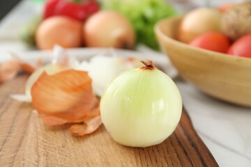 Wooden board with fresh onion and peels on table, closeup